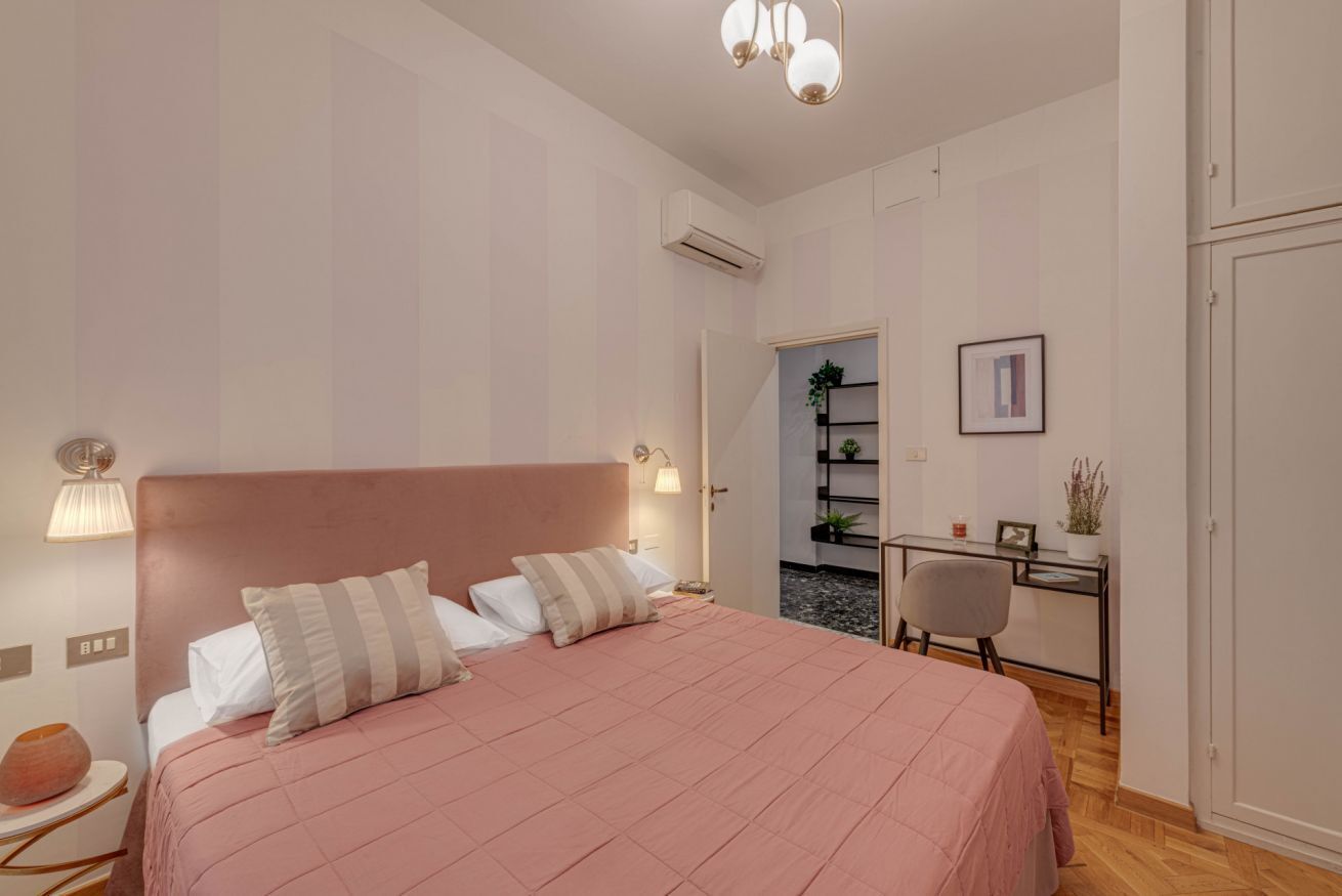 A bedroom with a bed, bedside lamps, a desk, and a chair.