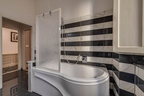 A modern bathroom with a freestanding bathtub, a shower enclosure, and a tiled wall with a marble pattern.