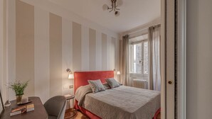 A hotel room with a bed, a desk, a chair, a potted plant, and a window with curtains. - Apartments Florence- Golden Tower with View (firenze)