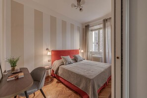 A hotel room with a bed, a desk, a chair, a potted plant, and a window with curtains. - Apartments Florence- Golden Tower with View (firenze)