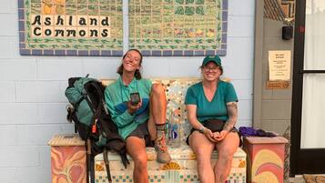 Two people sitting on a bench with backpacks, in front of a wall with a mosaic titled "Ashland Commons".