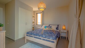 Ein Schlafzimmer mit Bett, Nachttischen, einer Hängelampe und einem Fenster.