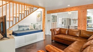 A living room with a brown leather sofa, a wooden staircase, and a view into the kitchen.