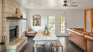 A cozy living room with a stone fireplace, a dining table, a leather couch, and a ceiling fan.