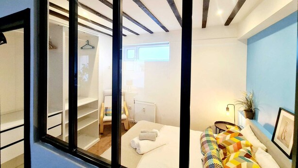 A modern hotel room with a large mirror, a bed with colorful pillows, a bedside table, and a view of the bathroom. - Luxury 2 bedrooms flat (Luxembourg City)