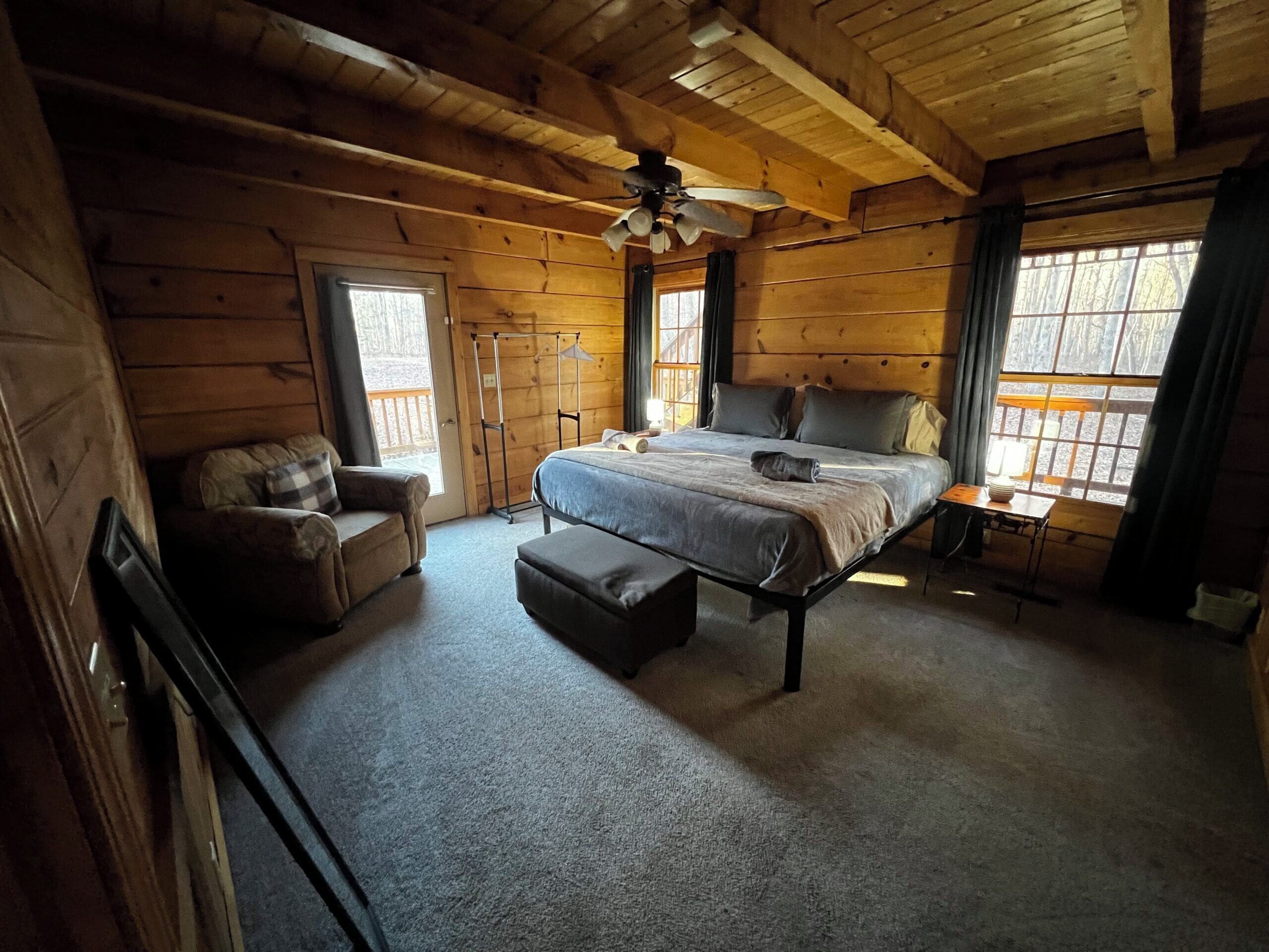 A cozy log cabin bedroom with a bed, a chair, a desk, and a window with curtains.