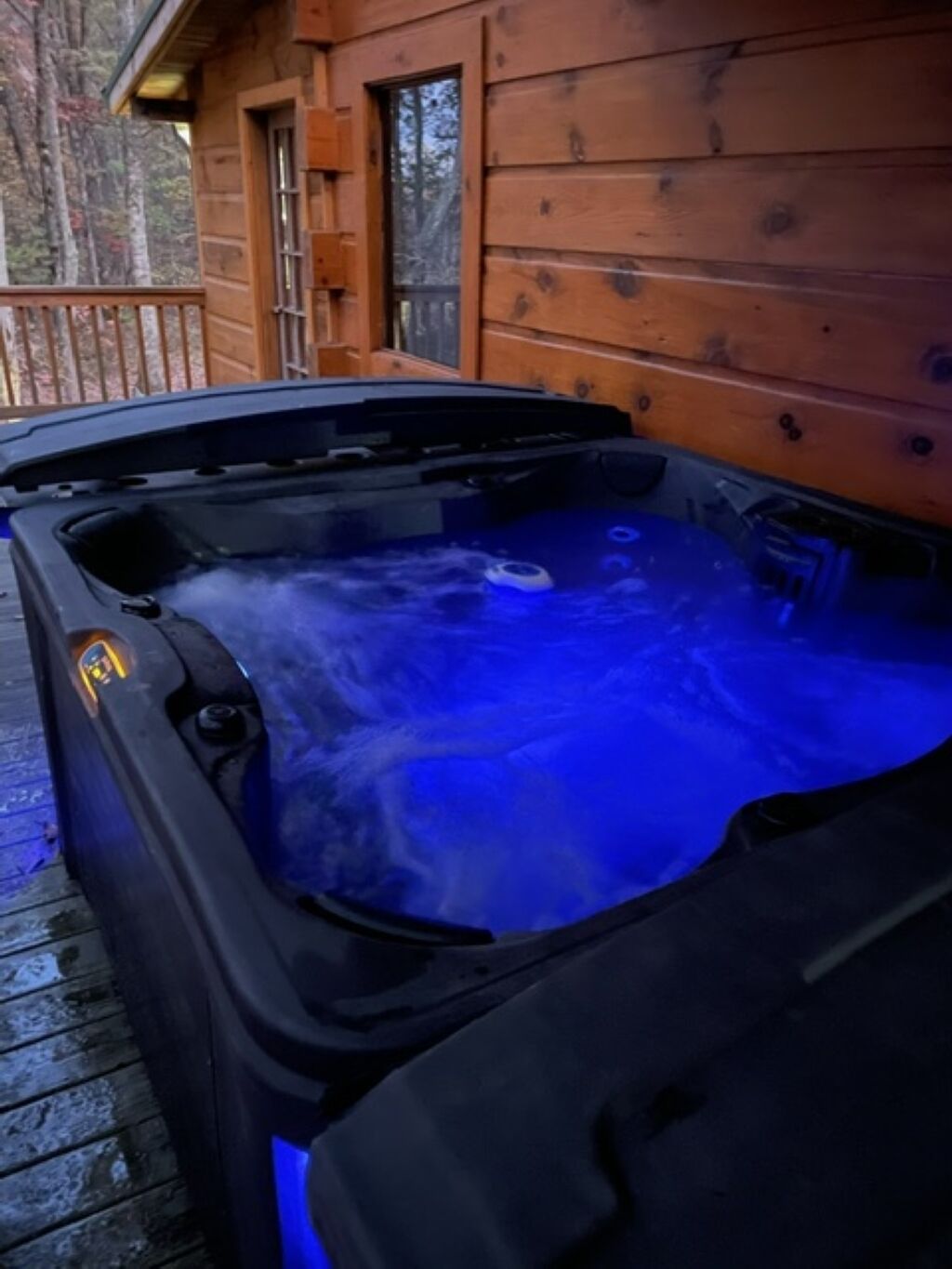 A hot tub with a blue light, surrounded by wooden deck and a cabin.