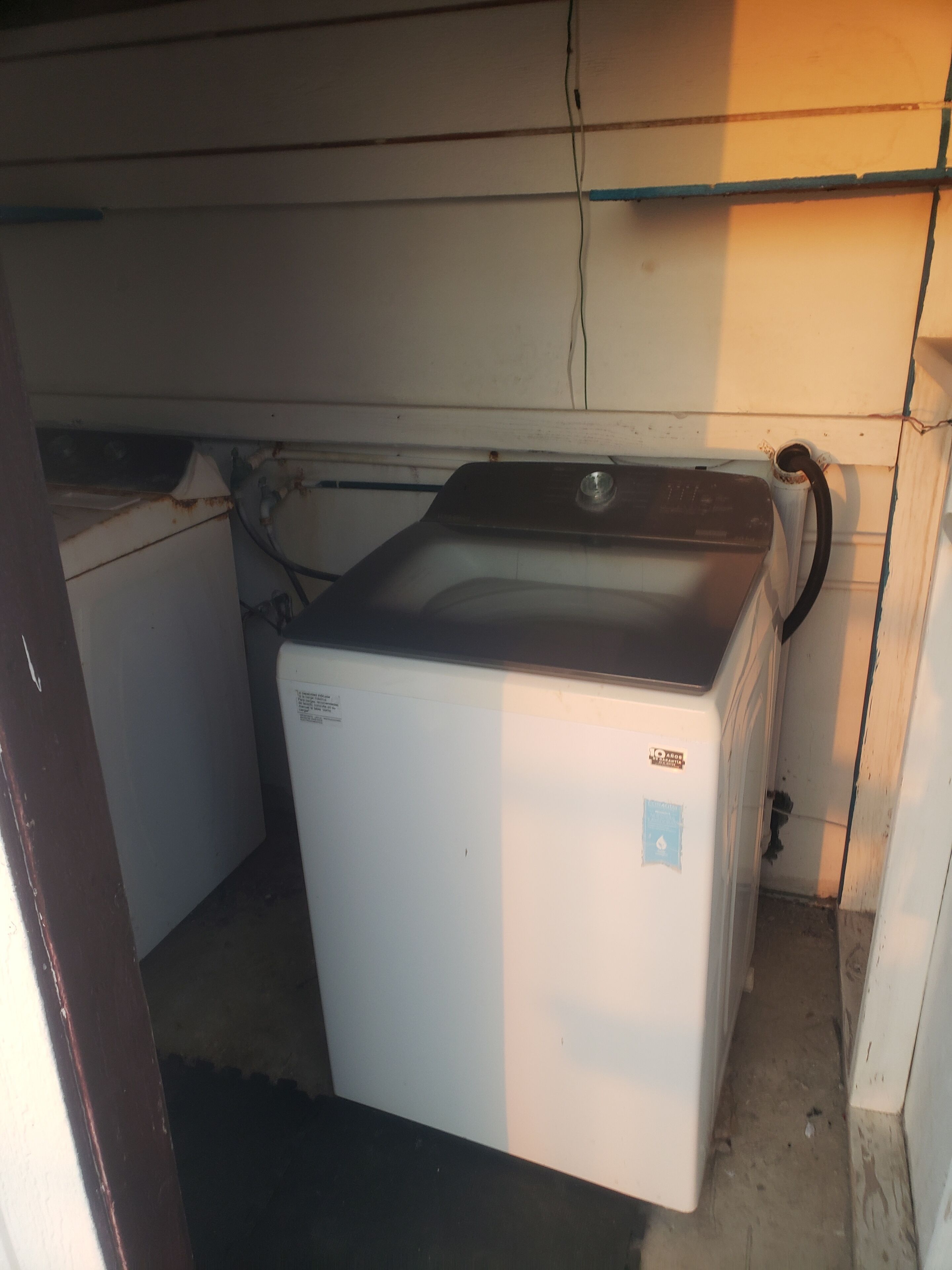 Een compacte, witte wasmachine in een kleine, zwak verlichte ruimte met een betonnen vloer en een scheur in de muur.