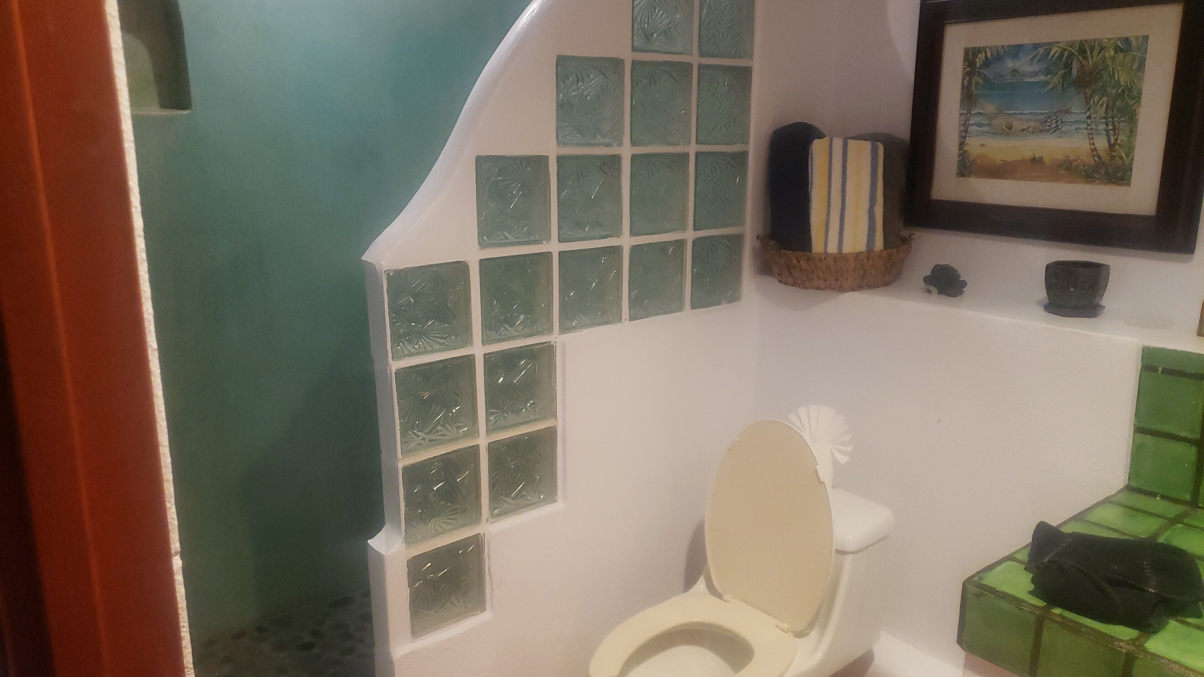 A bathroom with a toilet, a green tiled wall, a framed picture, and a basket on the wall.