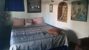 A bedroom with a bed, a blue curtain, a wall-mounted shelf with decorative items, and a painting. - Olas ocean suite, pool, jacuzzi, bbq & terrace..Pet friendly, gated & secure (Primo Tapia)