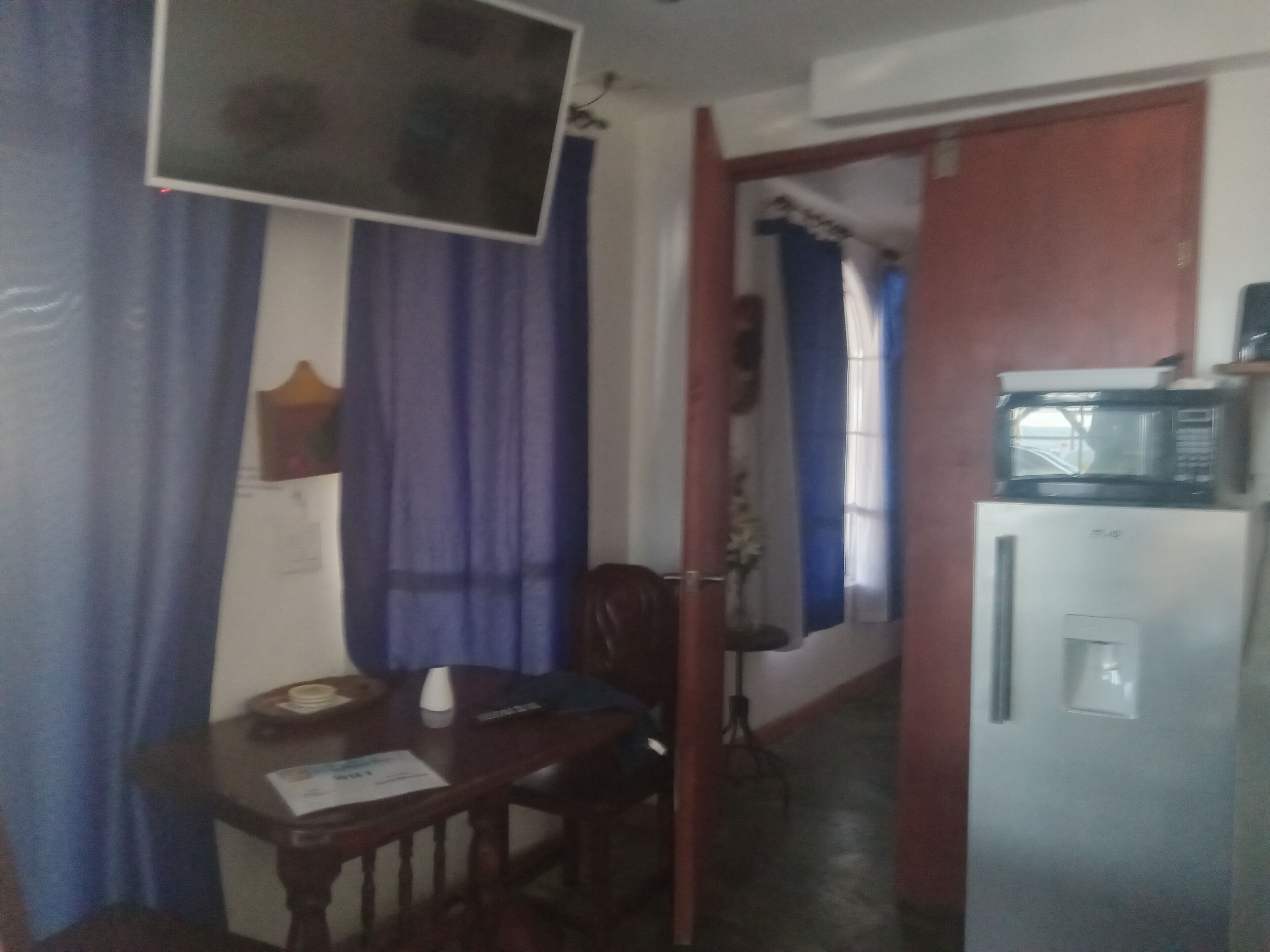 Une pièce comprenant une table à manger, des chaises, un téléviseur fixé au mur et un réfrigérateur sur lequel est posé un four à micro-ondes.