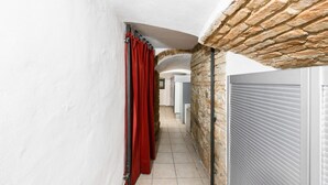 Um corredor estreito com parede de pedra, cortina vermelha e porta com persiana fechada.