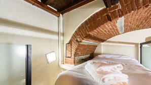 Quarto de hotel com arco de tijolos, cama com roupa de cama branca e mesa de cabeceira com abajur.