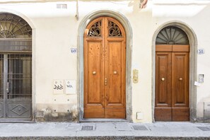 A building with two wooden double doors, each with a number above it, and a window with a metal grille to the left. - Pepi Red apartment in Florence by Mmega (Firenze)