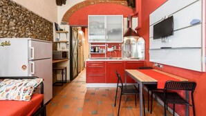 Cozinha compacta com geladeira, fogão e micro-ondas. Há uma área de refeições com mesa e cadeiras.