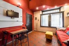 A compact room with a TV, a dining table, chairs, a sofa, a window, and a door. - Pepi Red apartment in Florence by Mmega (Firenze)