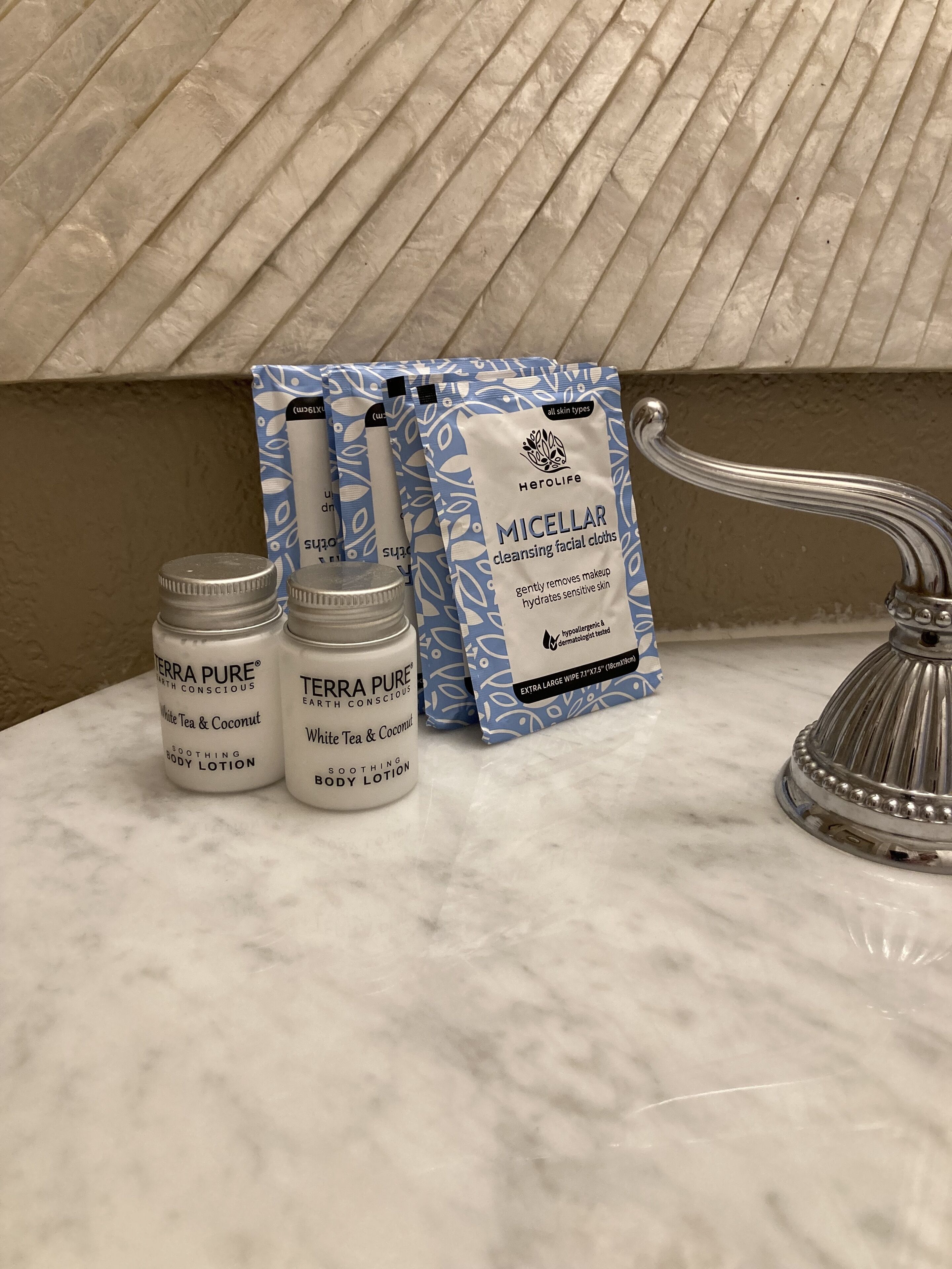 A bathroom counter with Terra Pure body lotion bottles, Herolife micellar cleansing facial cloths, and a silver faucet.