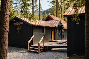 Une cabane dotée d’une terrasse en bois et d’un toit en métal, entourée d’arbres.
