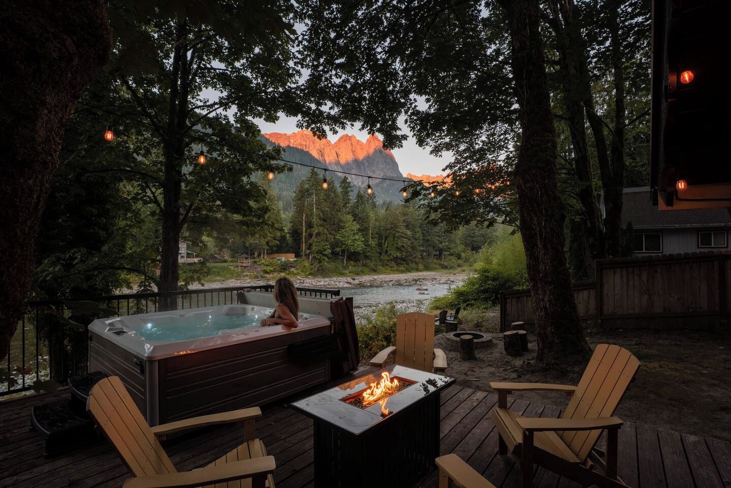 Tinaco con chimenea, rodeado de sillas de madera en una terraza, con vista a un río y montañas.