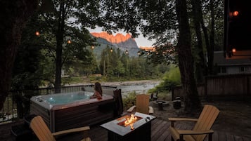 Tinaco con chimenea, rodeado de sillas de madera en una terraza, con vista a un río y montañas.