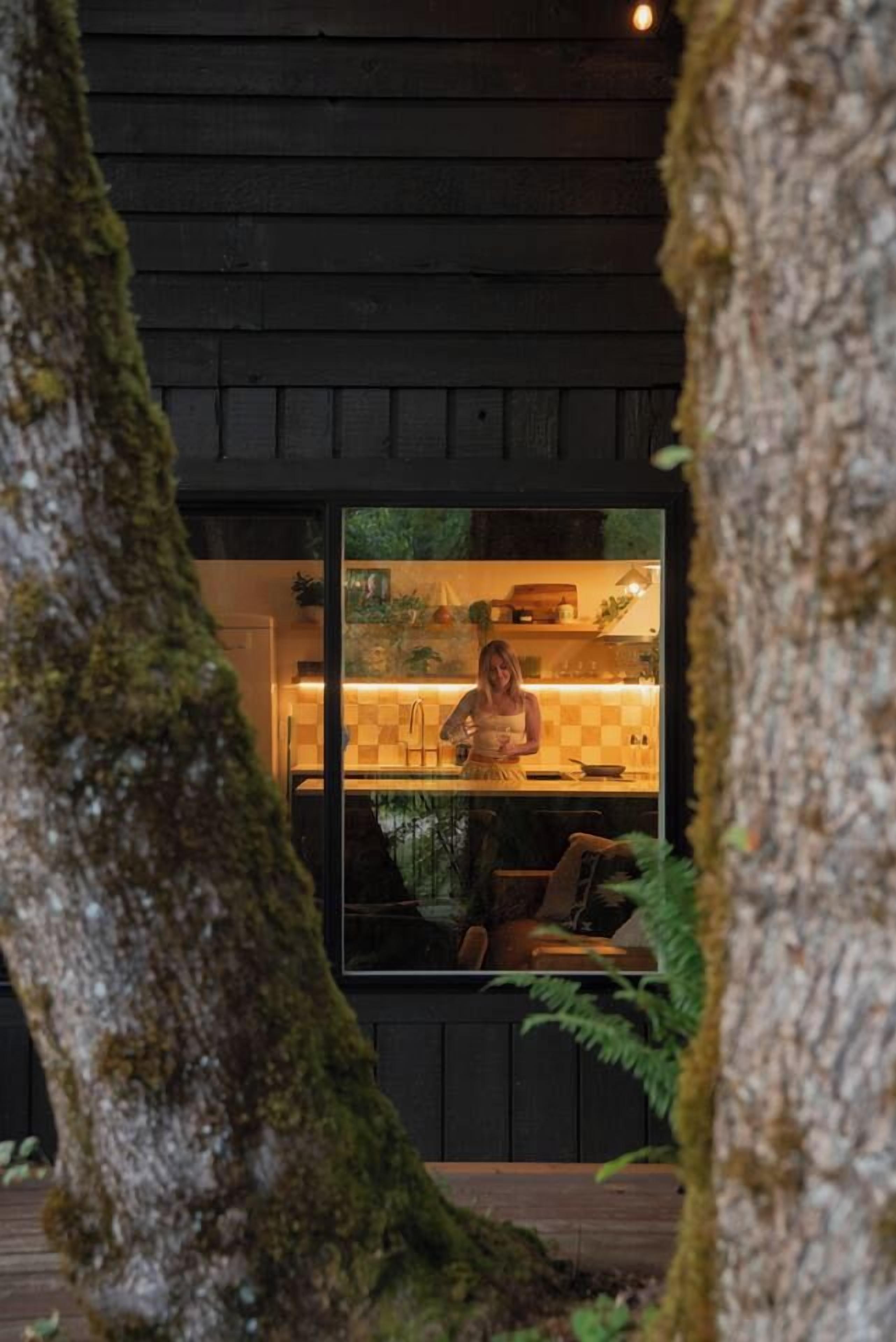 Una cocina moderna con una persona cocinando, rodeada de paredes de madera y un gran tronco de árbol.