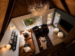 A loft-style living area with a wooden ceiling, a fireplace, a sofa set, a coffee table, and a chandelier.