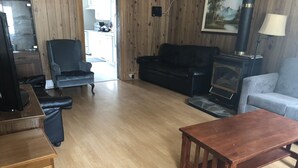 Ein Wohnzimmer mit Holzboden, einem schwarzen Ledersofa, einem blauen Sessel, einem Holztisch und einem Kamin.