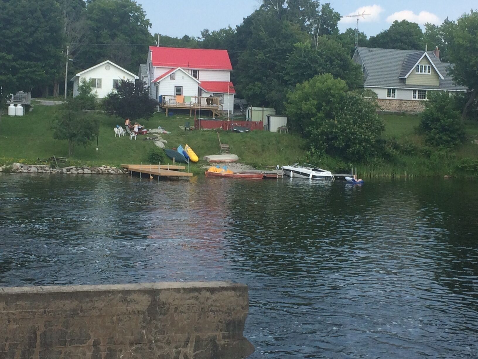 A lakeside scene with a dock, boats, and houses.