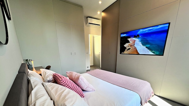 A modern bedroom with a bed, a TV mounted on the wall, and a wardrobe. - Appartement 7B - MyResidenced'Azur (Beausoleil)