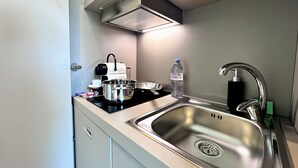 A compact kitchen with a stainless steel sink, a coffee maker, a kettle, and a bottle of water. - Appartement 7B - MyResidenced'Azur (Beausoleil)