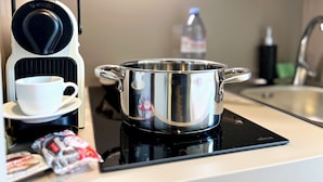 A kitchen with a coffee maker, a pot on an induction cooktop, a cup, and some snacks. - Appartement 7B - MyResidenced'Azur (Beausoleil)