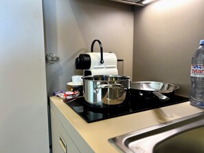Une petite cuisine équipée d’une cuisinière, de casseroles, d’une bouilloire, d’une machine à café et d’une bouteille d’eau.