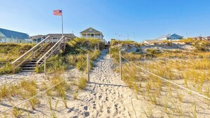 A sandy beach path leading to a house with a flag, surrounded by dunes and other beach houses. - A Shore Thing - Oceanfront - Hot Tub -Pet Friendly (Carolina Beach)