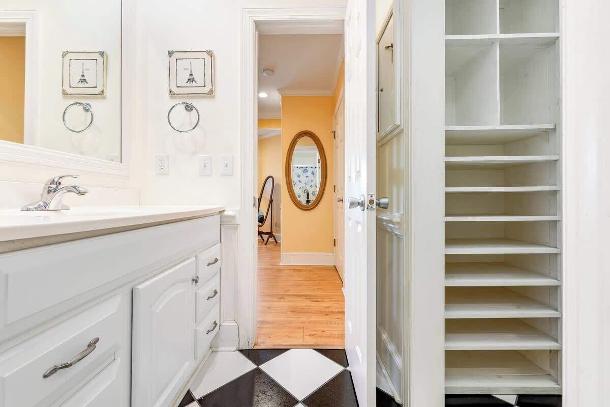 Un baño con tocador blanco, piso a cuadros blanco y negro, y vestidor con estantes.