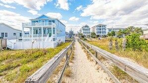 Una propiedad frente a la playa con una casa azul destacada, un camino de arena y una valla de madera.