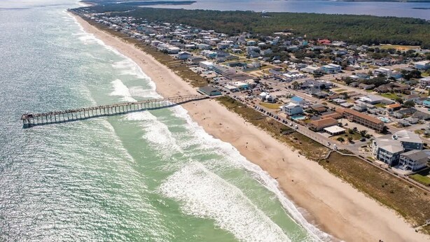 Une vue aérienne d’une ville côtière, avec une jetée qui s’avance dans l’océan, des propriétés situées en bord de mer et un ensemble dense de bâtiments.