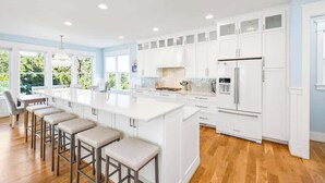 A spacious kitchen with white cabinetry, a large island with stools, and a built-in refrigerator. - Seaside Palace (Kure Beach)