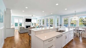 A spacious kitchen with a large island, white cabinetry, and a dining area with a white table and chairs. - Seaside Palace (Kure Beach)