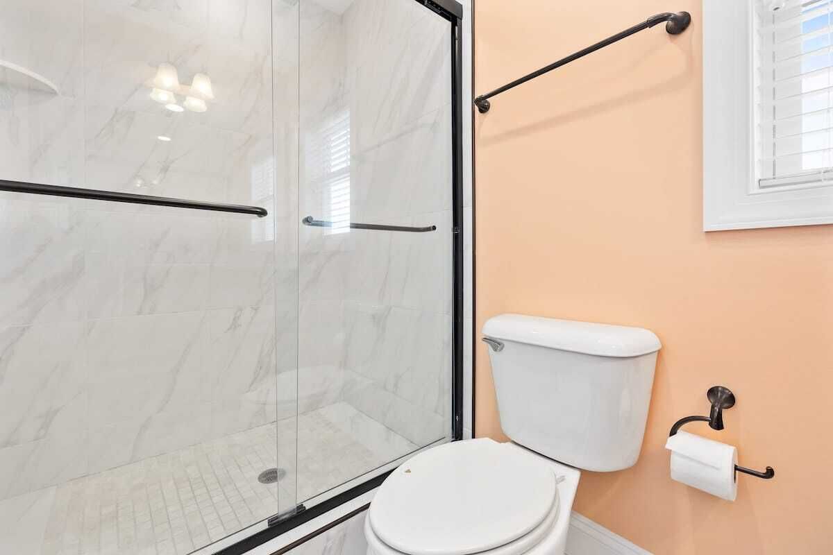 Une salle de bain avec une douche à parois de verre, des toilettes blanches et un porte-serviettes.