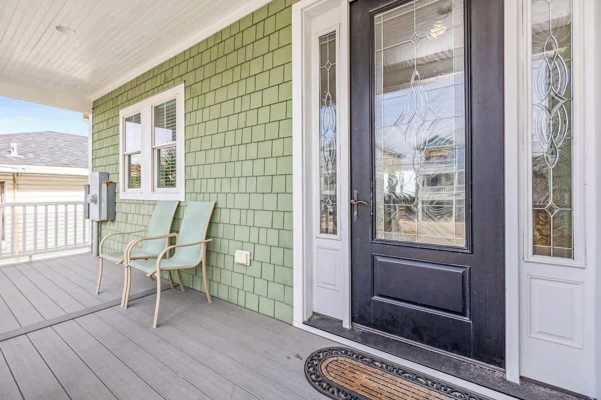 A porch with a green shingled exterior, a black front door with glass panels, and a metal bench.