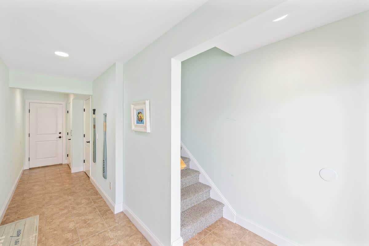 Un couloir avec un mur de couleur vert clair, une porte blanche et un escalier dont les marches sont recouvertes de moquette.