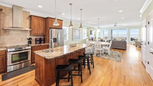 A spacious kitchen with a large island, stainless steel appliances, and pendant lighting. - No Cleaning Fee - 6BR Oceanfront - Oceanfront - Pool (Carolina Beach)