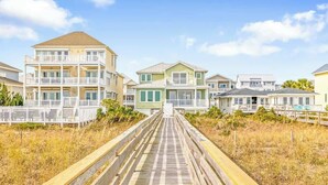 A wooden boardwalk leading to beachfront houses with balconies and a clear sky. - No Cleaning Fee - 6BR Oceanfront - Oceanfront - Pool (Carolina Beach)