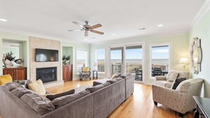 A spacious living room with a large sectional sofa, a smaller armchair, a flat-screen TV, and a fireplace. - No Cleaning Fee - 6BR Oceanfront - Oceanfront - Pool (Carolina Beach)