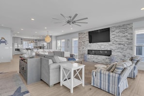 A spacious living area with a fireplace, a large TV, and a ceiling fan.
