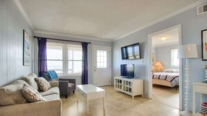 Un salon avec un canapé, une table basse, un téléviseur posé sur un meuble et un lit dans la pièce adjacente.