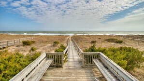 Une promenade en bois menant à la plage, avec un ciel dégagé au-dessus.