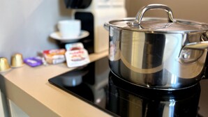Eine Küchenzeile mit einem Edelstahlkochtopf auf einer schwarzen Induktionskochplatte, einer Kaffeemaschine und einer weißen Tasse auf einem Untertasse.