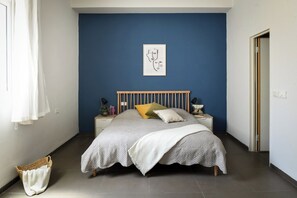 A bedroom with a bed, a bedside table, a wall art piece, and a window with curtains. - The Printhouse Boutique Studio 5 by SeaNRent (Haifa)