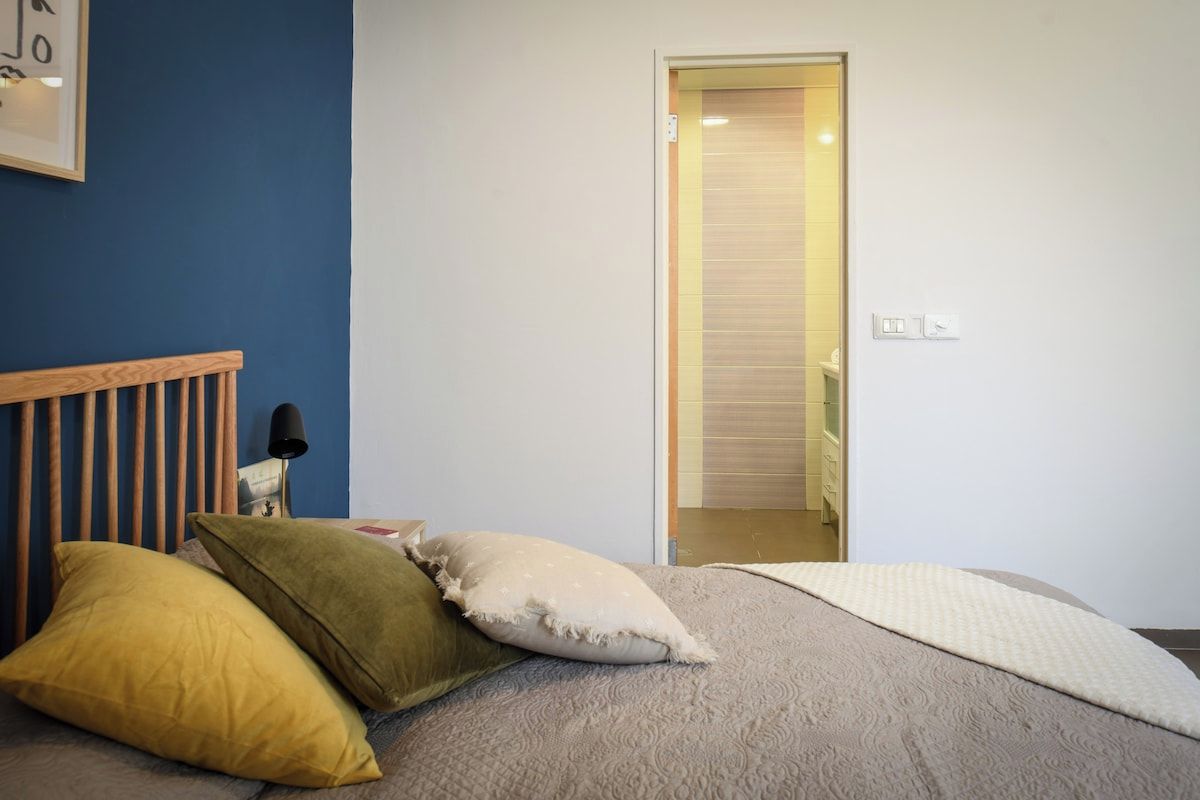 Ein Schlafzimmer mit Bett, Kissen, einer Nachttischlampe und einer Tür zu einem Badezimmer.